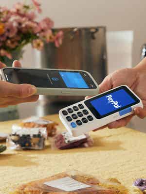 Cliente haciendo una transacción con su celular en un lector de tarjetas blanco PayPal