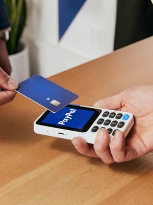 Un vendedor sosteniendo un lector de tarjetas blanco de PayPal para que un cliente pague con tarjeta