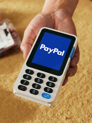 El dueño de una tienda sosteniendo un lector de tarjetas con el logo de PayPal en una pantalla azul