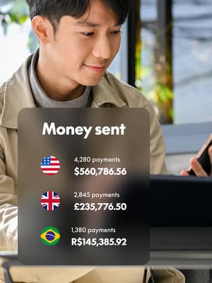 Person working on laptop computer and holding phone with overlay of Money sent in different currencies