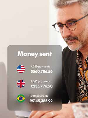 Person working on laptop computer and holding phone with overlay of Money sent in different currencies