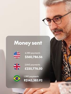 Person working on laptop computer and holding phone with overlay of Money sent in different currencies