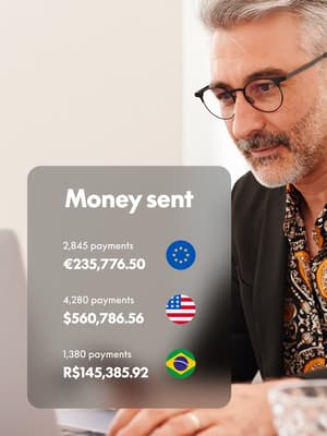 A man works on his laptop computer with an overlay of a Money Sent screen showing denominations from the EU, the USA, and Brazil. 