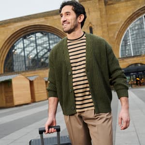 Man wearing green sweater is smiling and sightseeing as he carries his luggage