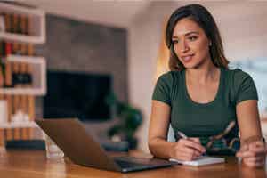 A woman in front of a laptop taking notes about her credit score and how to improve it