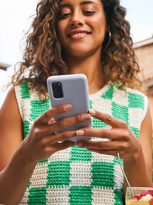 Image alt text: Smiling woman using a smartphone outdoors in a sunny neighborhood.