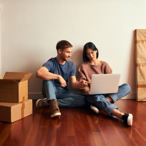 Two people sitting on floor surrounded by cardboard boxes