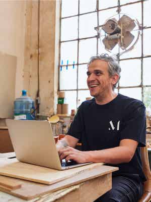 Smiling business owner managing a dispute on his laptop in his woodworking shop