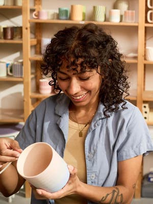 A woman smiles while shaping a ceramic cup.