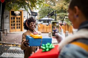 A woman smiles while giving gifts to a friend