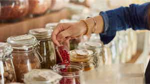 A hand shopping for spices, putting a red spice in a plastic bag to purchase.