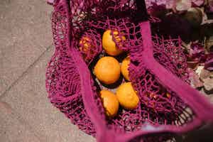 A purple mesh produce bag filled with oranges.