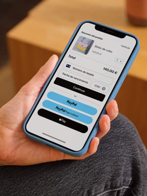 Persona sosteniendo teléfono móvil mostrando pantalla de pago con opciones de pago incluyendo tarjeta de débito/crédito, PayPal, Paga a plazos y Apple Pay