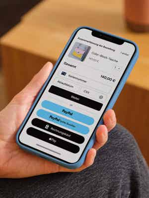 Eine Person hält ein Mobiltelefon in der Hand, das den Kassenbildschirm mit Zahlungsoptionen wie Debit-/Kreditkarte, PayPal, Pay Later und Apple Pay anzeigt.