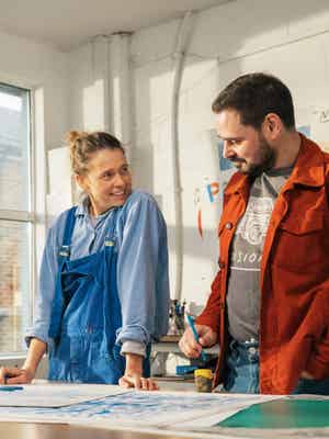 Frau und Mann, die in einer Werkstatt vor einem Schreibtisch stehen