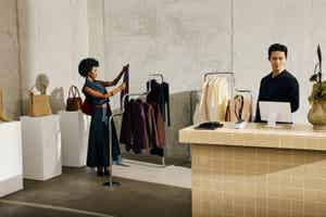 A young woman holds clothes in boutique with both hands and looks at it