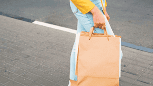 Person carrying a brown paper shopping bag while walking outdoors.