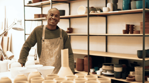Smiling ceramic artist standing in a pottery studio surrounded by handmade pottery and ceramics.
