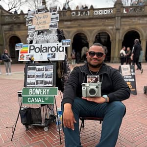 Martin Fermin, founder of Polaroids NYC, sitting at his instant photo stand near Bethesda Fountain in Central Park.