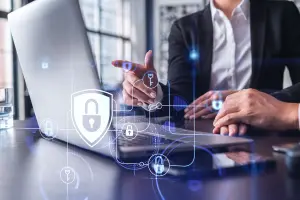 Two business professionals reviewing a laptop, with digital shield, lock, and key icons overlaid to represent transaction security and fraud protection.
