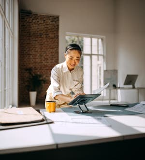 A standing woman works from a mobile tablet in an office.