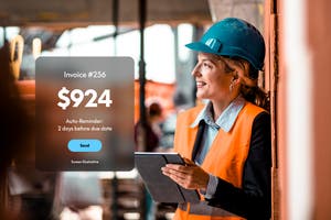 Construction worker in safety gear holding a tablet on site, with an invoice reminder screen displayed in the foreground.