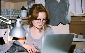 Woman working at a laptop in a tailoring studio.