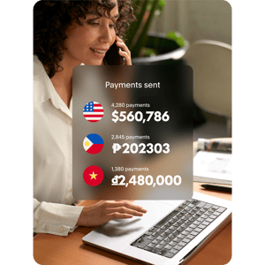 An image showing a woman working on her laptop with an overlay showing that she’s paying suppliers across the globe