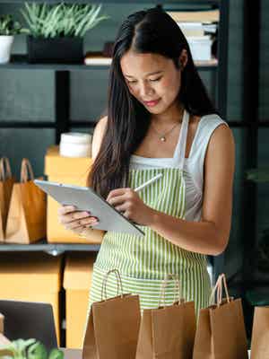 Woman writing on tablet in front of four paper bags