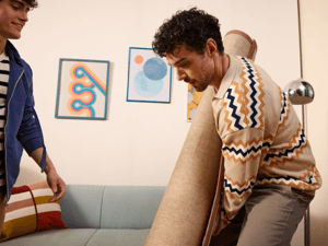 Two men in patterned shirts moving a rug into a living space.