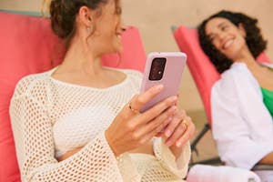 International traveler makes a cross-border payment while sitting in a lounge chair with a friend.