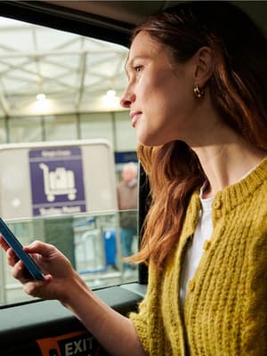 A woman sitting in a taxi outside an airport terminal looks out the window while holding a smartphone in her hand